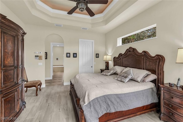 bedroom featuring light wood-type flooring, ceiling fan, ornamental molding, and a tray ceiling