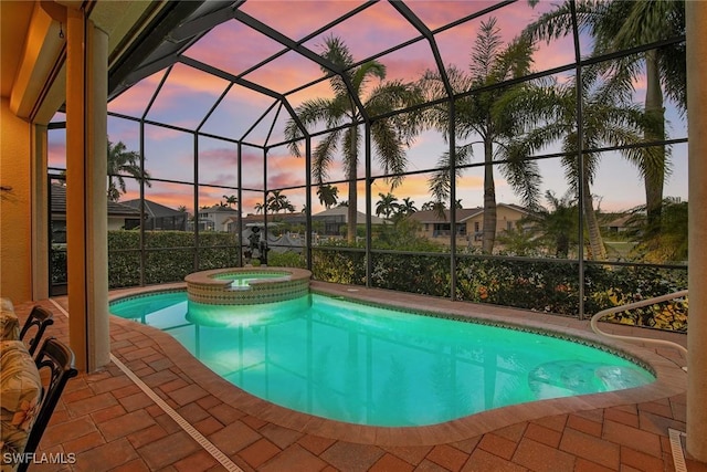 pool at dusk featuring an in ground hot tub, glass enclosure, and a patio area