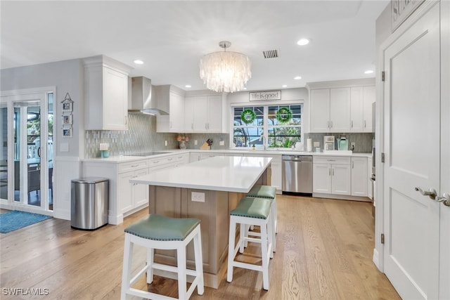 kitchen with wall chimney exhaust hood, a breakfast bar, white cabinetry, hanging light fixtures, and stainless steel dishwasher