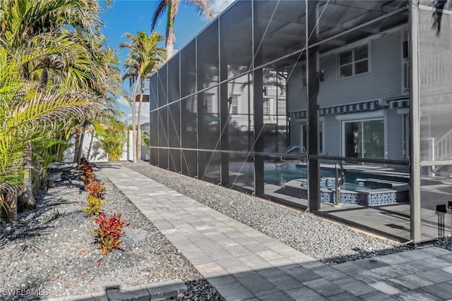 view of property exterior with a swimming pool with hot tub, a patio, and glass enclosure