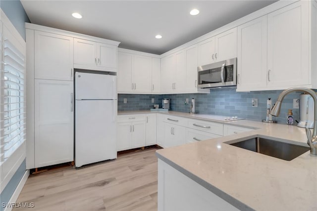 kitchen featuring sink, white refrigerator, light stone countertops, light hardwood / wood-style floors, and white cabinets