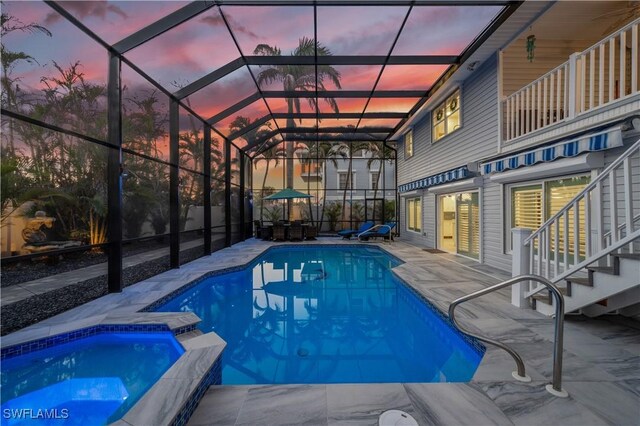 pool at dusk with an in ground hot tub, a patio area, and glass enclosure