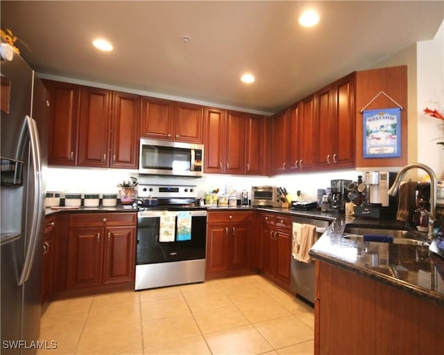 kitchen with sink, light tile patterned flooring, dark stone counters, and appliances with stainless steel finishes