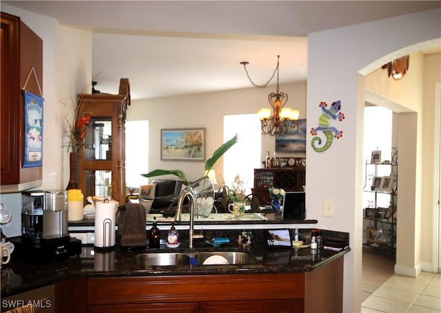 kitchen featuring pendant lighting, an inviting chandelier, dark stone counters, light tile patterned flooring, and sink