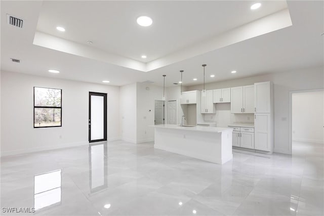 kitchen featuring sink, hanging light fixtures, an island with sink, white cabinets, and a raised ceiling