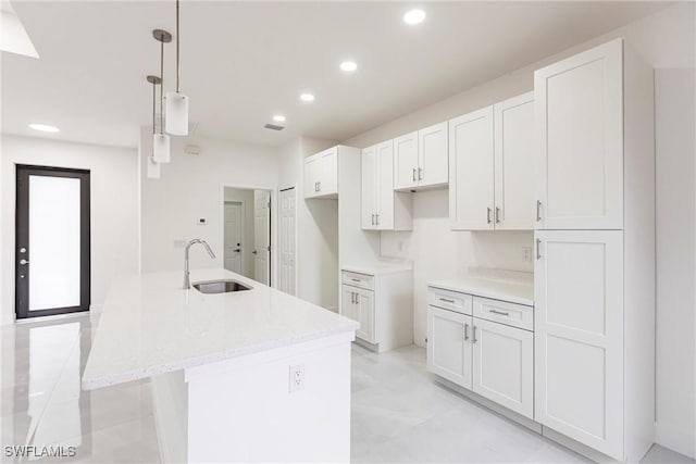 kitchen with white cabinetry, a kitchen island with sink, sink, and hanging light fixtures