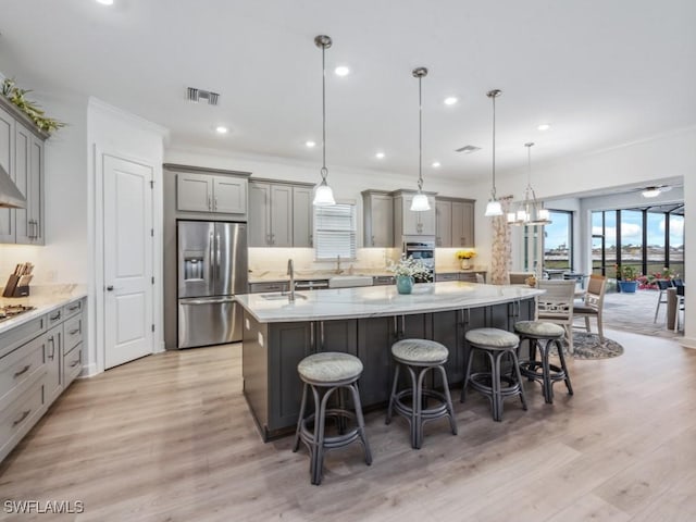 kitchen with gray cabinets, a breakfast bar area, stainless steel fridge, hanging light fixtures, and a center island with sink