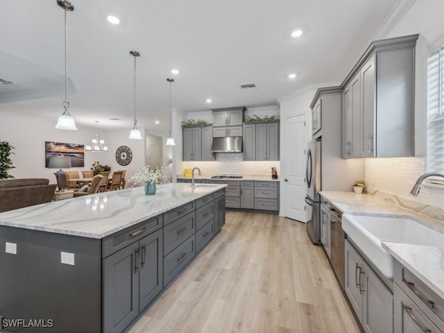 kitchen featuring appliances with stainless steel finishes, gray cabinetry, light stone countertops, decorative light fixtures, and a large island with sink