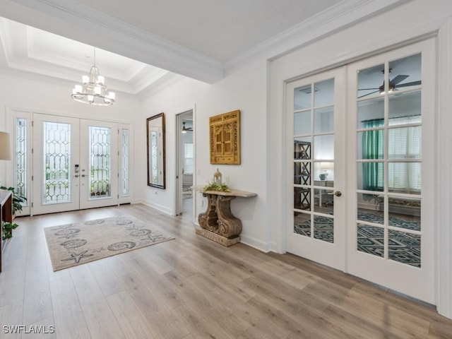 foyer featuring french doors, crown molding, a tray ceiling, a notable chandelier, and hardwood / wood-style flooring