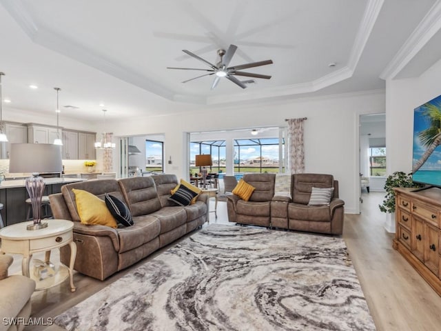 living room featuring crown molding, ceiling fan with notable chandelier, a raised ceiling, and light hardwood / wood-style floors