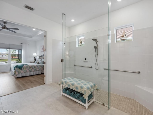 bathroom featuring a tile shower, ceiling fan, a raised ceiling, and a healthy amount of sunlight