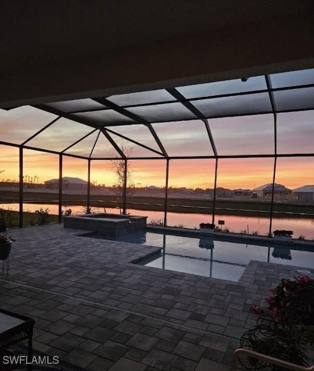 patio terrace at dusk featuring a swimming pool with hot tub, a water view, and glass enclosure