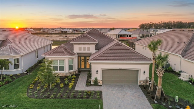 15745 Cortina St, Naples, FL 34114 - view of front of property featuring an attached garage, a tiled roof, decorative driveway, stucco siding, and stone siding