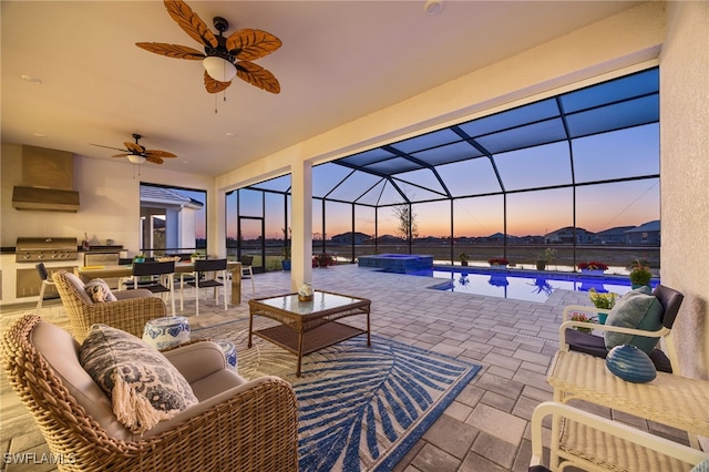 patio terrace at dusk featuring a grill, a lanai, exterior kitchen, and a pool with hot tub