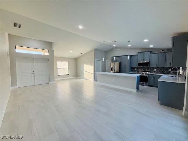 kitchen featuring stainless steel appliances, sink, vaulted ceiling, backsplash, and a kitchen island