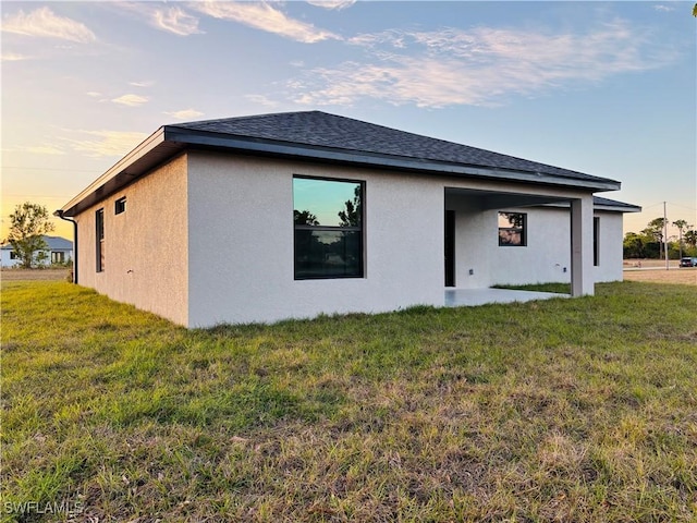 back house at dusk featuring a lawn