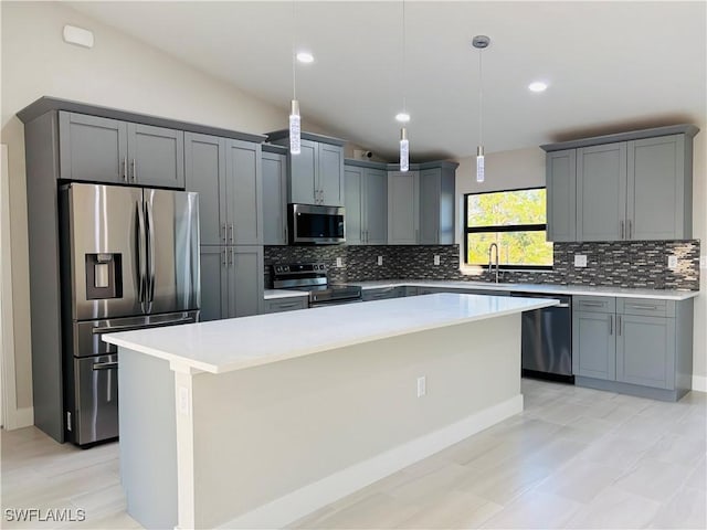 kitchen with vaulted ceiling, pendant lighting, a kitchen island, gray cabinets, and appliances with stainless steel finishes