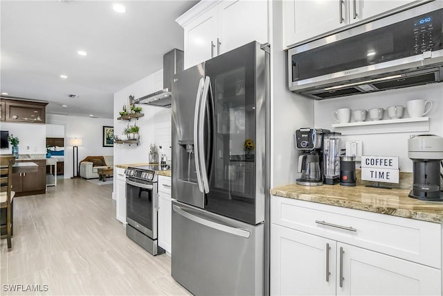 kitchen with stainless steel appliances, light stone countertops, white cabinets, and wall chimney exhaust hood