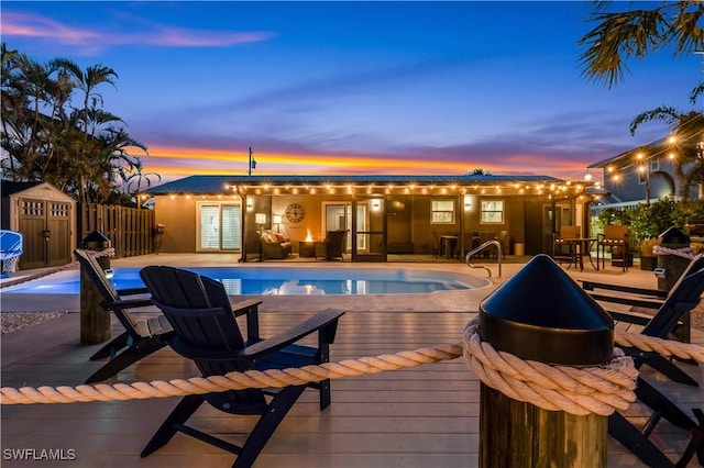 pool at dusk with a deck and a storage shed