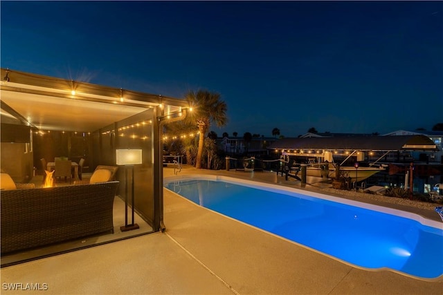 pool at night featuring outdoor lounge area and a patio area