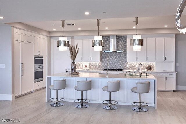 kitchen featuring decorative light fixtures, wall chimney range hood, and a center island with sink