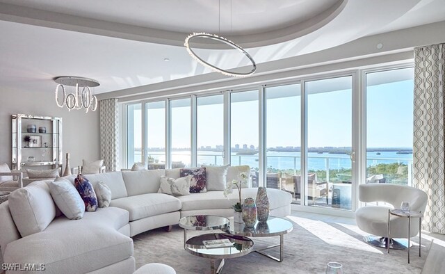 living room with a water view, an inviting chandelier, and a tray ceiling