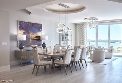 dining space featuring a chandelier, a tray ceiling, light hardwood / wood-style flooring, and a water view