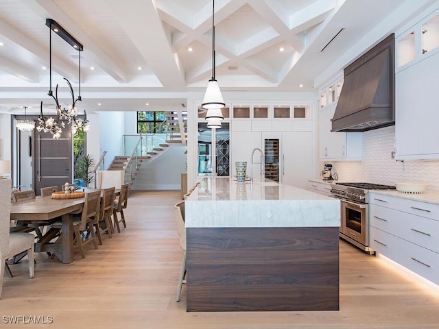 kitchen featuring high end range, a spacious island, beamed ceiling, hanging light fixtures, and custom range hood