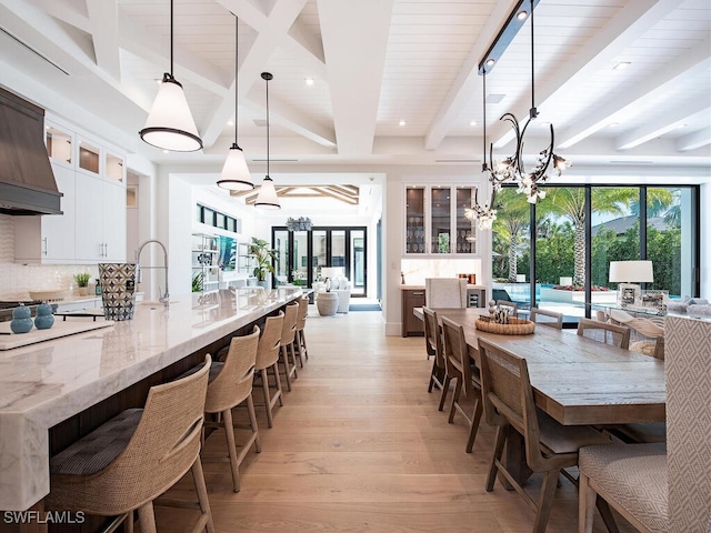 interior space with pendant lighting, beam ceiling, light wood-type flooring, white cabinets, and light stone counters