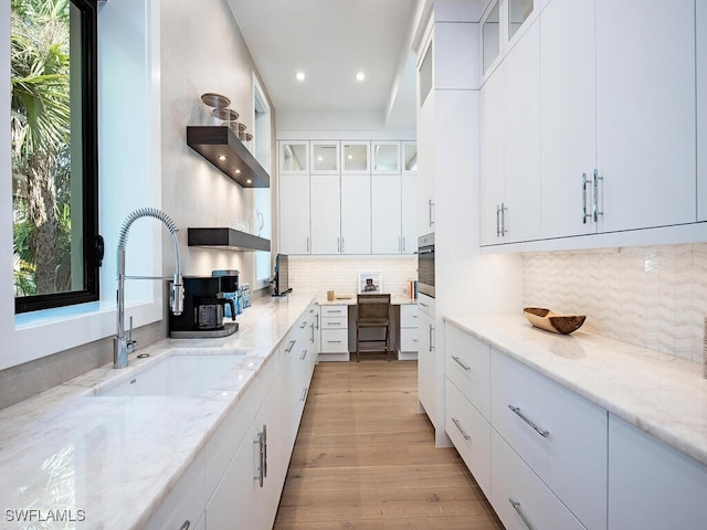 kitchen with stainless steel oven, white cabinets, light stone countertops, and sink