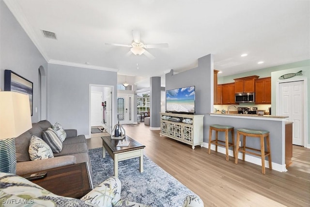 living room with crown molding, ceiling fan, sink, and light hardwood / wood-style flooring