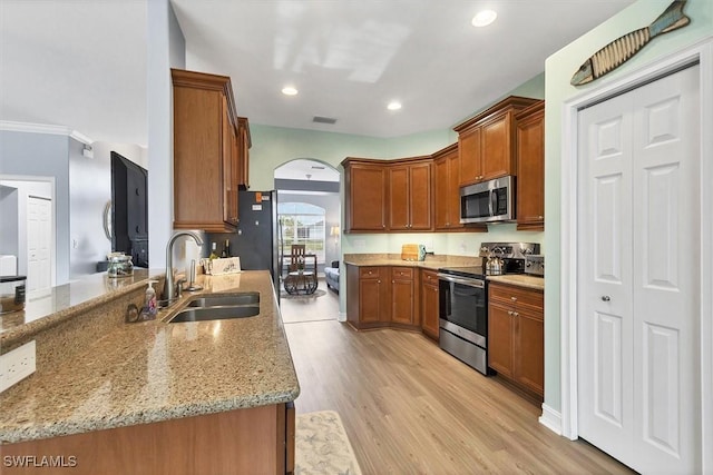 kitchen featuring sink, light stone countertops, light hardwood / wood-style floors, and appliances with stainless steel finishes