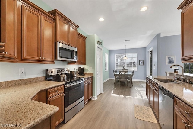 kitchen featuring appliances with stainless steel finishes, pendant lighting, sink, light stone counters, and light hardwood / wood-style flooring