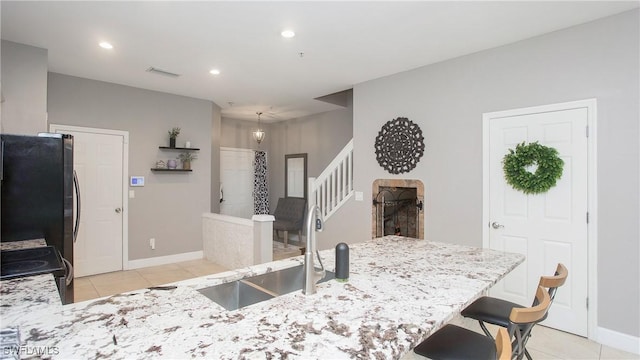 kitchen with range with electric stovetop, stainless steel fridge, light tile patterned floors, a breakfast bar, and sink