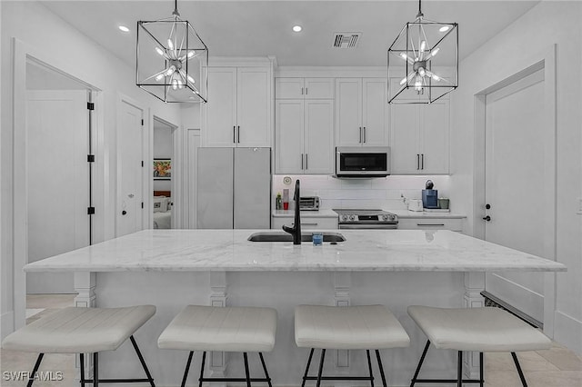 kitchen with white cabinetry, a center island with sink, appliances with stainless steel finishes, hanging light fixtures, and sink