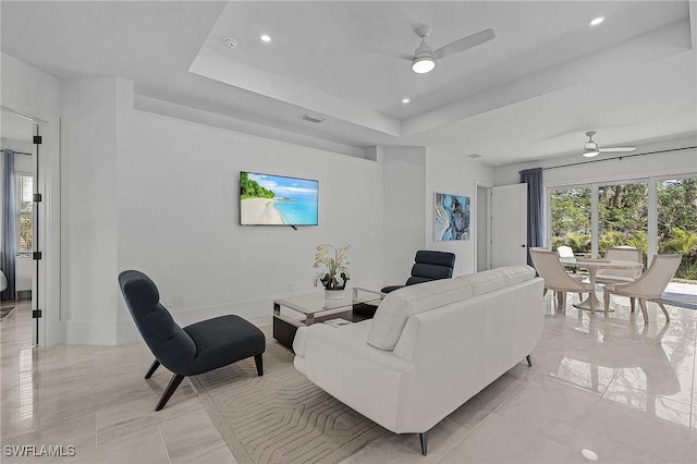 living room with ceiling fan, a raised ceiling, and a healthy amount of sunlight