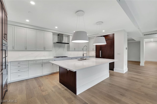 kitchen with decorative light fixtures, an island with sink, sink, gas cooktop, and wall chimney range hood