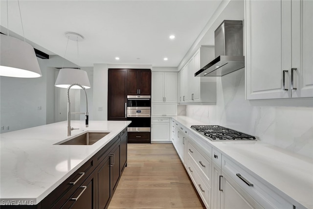 kitchen featuring dark brown cabinetry, white cabinetry, decorative light fixtures, appliances with stainless steel finishes, and wall chimney range hood