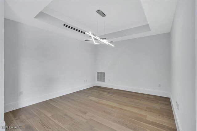 unfurnished room featuring a notable chandelier, light hardwood / wood-style floors, and a raised ceiling