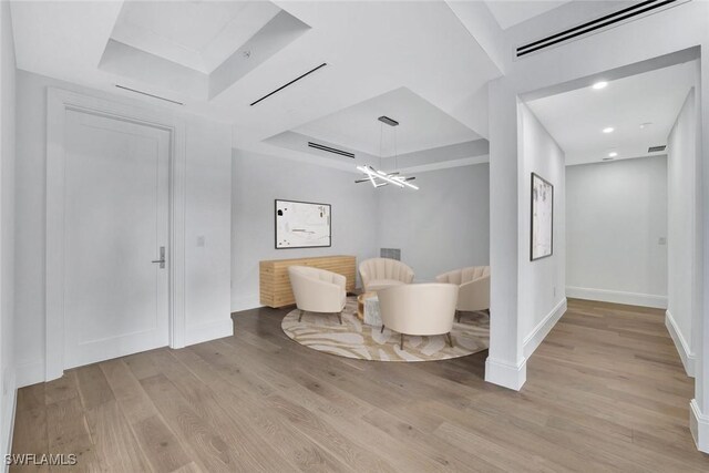 sitting room with an inviting chandelier, light hardwood / wood-style floors, and a tray ceiling