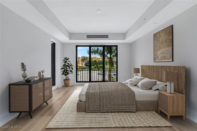 bedroom with a tray ceiling, access to outside, and light wood-type flooring