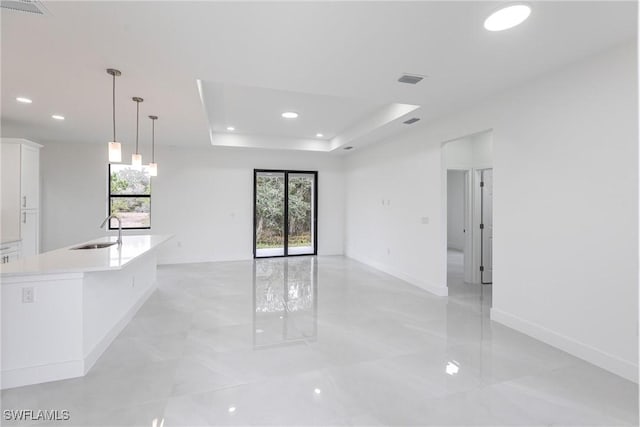 unfurnished living room with a healthy amount of sunlight, sink, and a tray ceiling