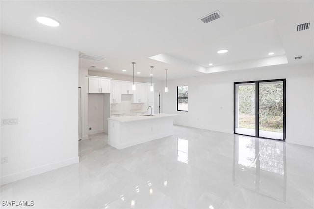 kitchen featuring decorative light fixtures, white cabinetry, a kitchen island with sink, and a tray ceiling