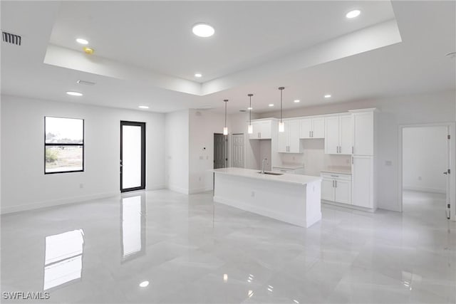 kitchen featuring white cabinetry, a kitchen island with sink, sink, and a tray ceiling