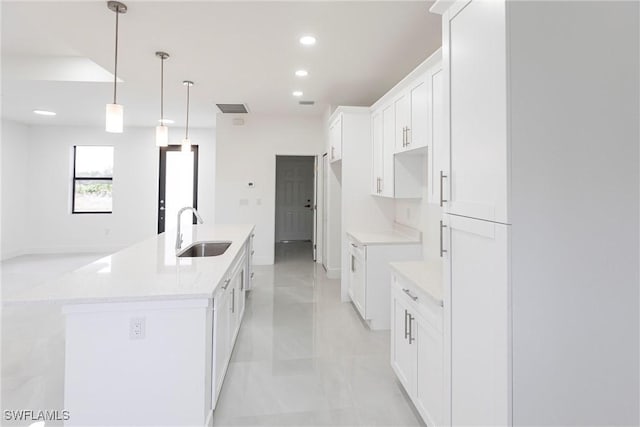 kitchen with a kitchen island with sink, sink, hanging light fixtures, and white cabinets