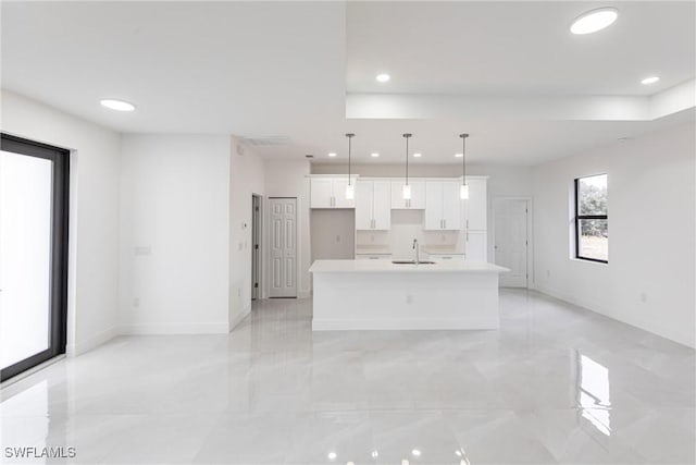 kitchen featuring hanging light fixtures, white cabinetry, sink, and a center island with sink