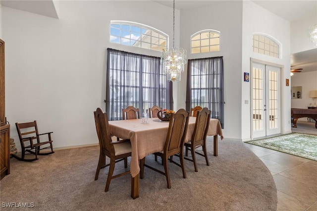 dining area featuring an inviting chandelier, tile patterned floors, a towering ceiling, and french doors