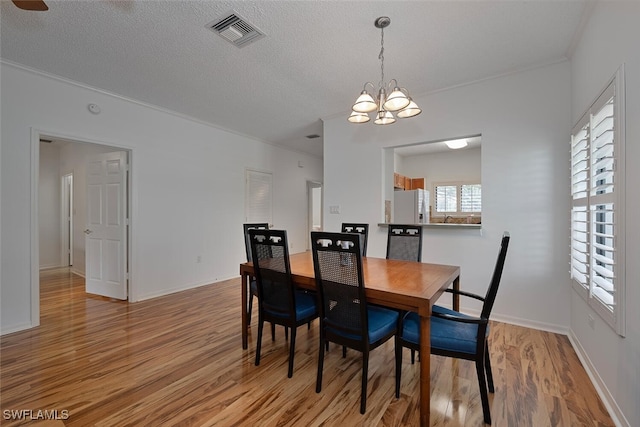 dining area featuring light wood-type flooring, an inviting chandelier, and a textured ceiling