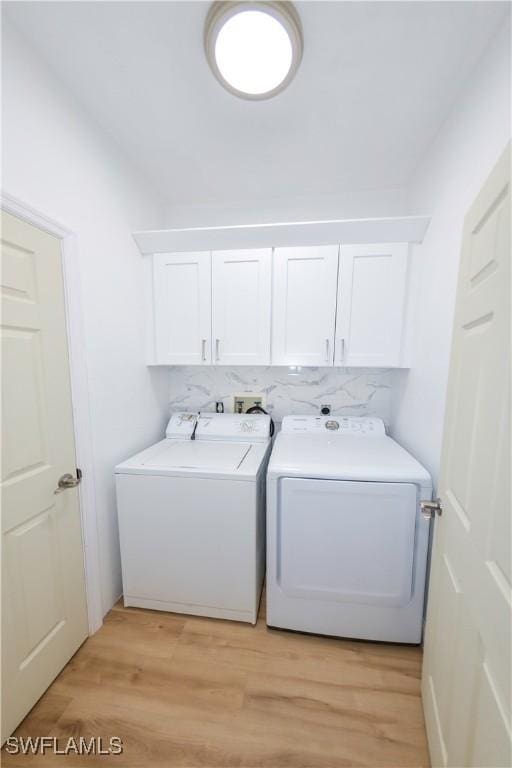 laundry room with light hardwood / wood-style flooring, separate washer and dryer, and cabinets