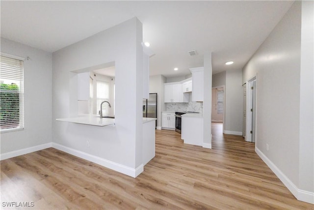 kitchen featuring light hardwood / wood-style floors, backsplash, white cabinets, and appliances with stainless steel finishes